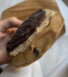 a person holding a chocolate covered doughnut in their hand