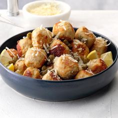 a blue bowl filled with meatballs covered in parmesan cheese and garnished with lemon wedges