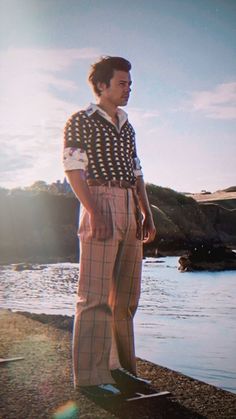 a man standing on the edge of a body of water with his hands in his pockets