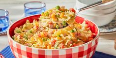 a red and white checkered bowl filled with macaroni, peas, ham and pasta