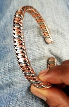 a woman's hand is holding onto a silver and gold bracelet that has been made from metal