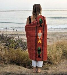 a woman is standing on the beach wrapped in a blanket with an image of two birds