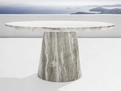 a white marble table sitting on top of a white floor next to a body of water