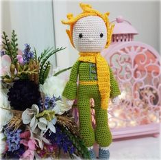 a crocheted doll sitting on top of a table next to flowers and a birdcage