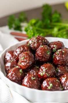 a white bowl filled with meatballs covered in sauce and garnished with parsley