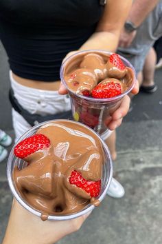 two people holding cups with chocolate and strawberries in them