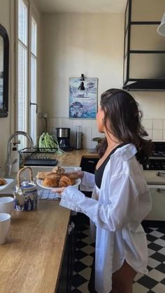 a woman standing at a kitchen counter holding a plate of doughnuts and looking out the window