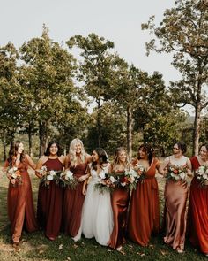 a group of women standing next to each other in front of trees with bouquets