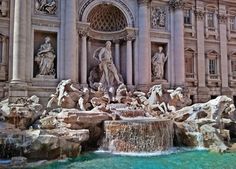 a fountain in front of a large building with statues on it's sides and water cascading