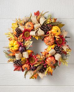 a wreath with fall leaves, pine cones and pumpkins hanging on a white wall