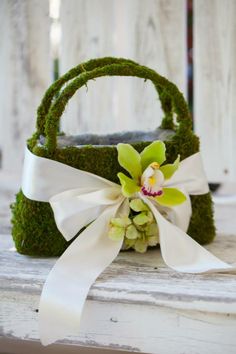 a basket with moss and flowers on it sitting on a table next to a white ribbon