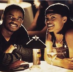 a man and woman sitting at a table with drinks in front of them, smiling