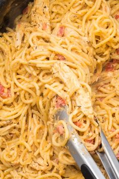 a pot filled with pasta and meat on top of a stove next to two tongs