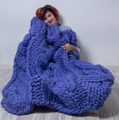 a woman laying on the floor wrapped in a large chunky knitted blanket,