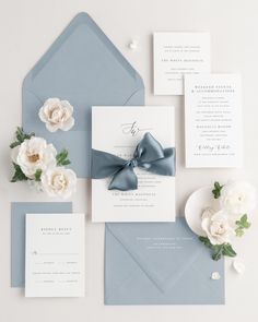 the wedding stationery is laid out on top of blue envelopes and white flowers