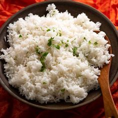 white rice in a bowl with a wooden spoon on an orange cloth covered tablecloth