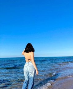 a woman standing on top of a sandy beach next to the ocean under a blue sky