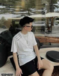 a young man sitting on top of a bench next to a glass wall with trees in the background