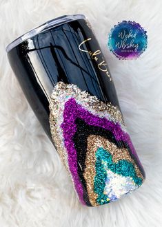 a black tumbler with purple, blue and gold glitters on the side sitting on a white furnishing