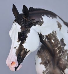 a black and white horse statue with brown spots on it's face, standing in front of a gray background