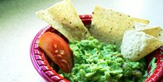 a red bowl filled with guacamole and tortilla chips on top of it