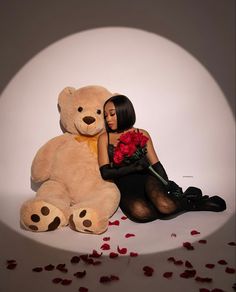 a woman sitting next to a giant teddy bear with roses on the floor in front of her