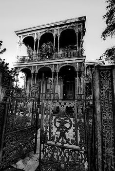 black and white photograph of an old building with iron gates in the foreground, surrounded by trees