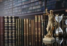 a statue of lady justice holding an hourglass in front of a library full of books