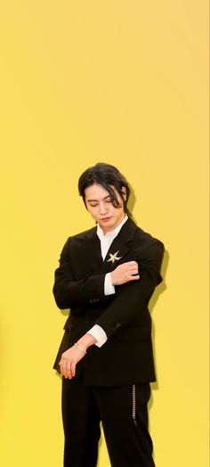 a man in a suit and tie standing with his arms folded over his chest against a yellow wall