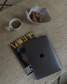 an apple laptop sitting on top of a table next to a bowl of cereal and a cup of coffee