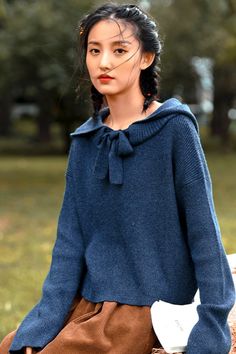 a woman sitting on top of a wooden bench wearing a blue sweater and brown pants