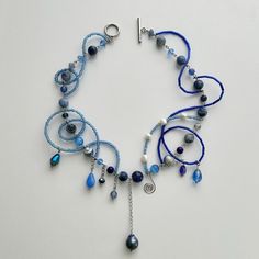 a necklace with blue beads and silver chains on a white surface, hanging from it's side