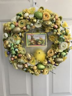 a wreath is hanging on the front door decorated with easter eggs, flowers and chicks