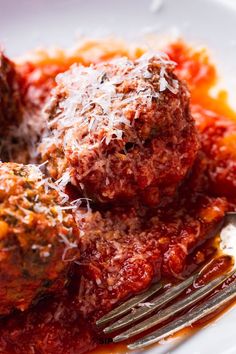 meatballs covered in sauce and parmesan cheese on a plate with a fork