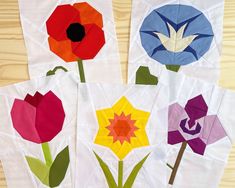 four pieces of paper with flowers on them sitting on a wooden table next to each other