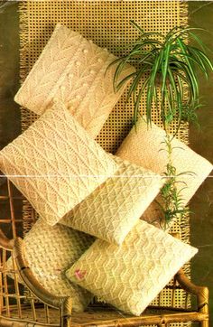 knitted pillows are arranged on a wicker chair with a potted plant in the corner