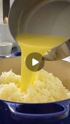 a person pouring yellow liquid into a blue pot filled with rice and other food items