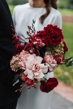 a bride and groom standing next to each other holding red and pink flowers in their hands