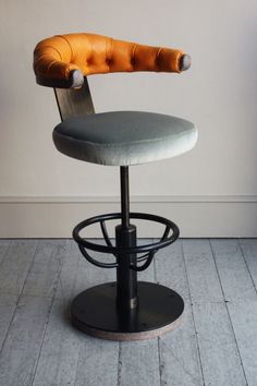 an upholstered stool with a curved seat and foot rest in front of a white wall