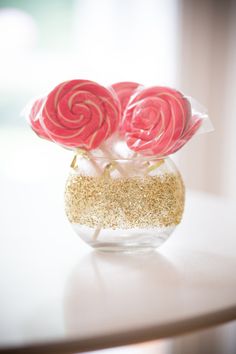 two lollipops in a glass vase with gold glitter on the side table