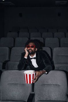 a man in a tuxedo sitting on a chair with a popcorn cup by luma studio for stockstation