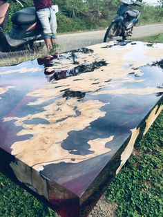 a motorcycle parked next to a large wooden table on the side of a dirt road