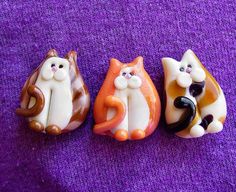 three cat figurines sitting next to each other on a purple surface