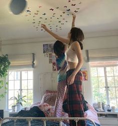 two women standing on top of a bed with paper butterflies hanging from the ceiling above them