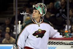 a hockey player is standing in front of the net with water splashing out of his face