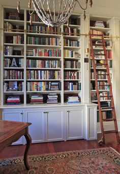 a living room filled with lots of books and a chandelier hanging from the ceiling