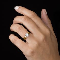 a woman's hand wearing a gold ring with a white diamond on the middle