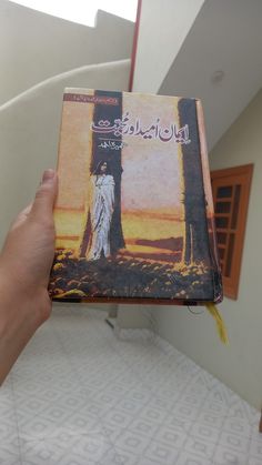 a person holding up a book in front of a spiral stair case with arabic writing on it