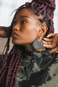 a woman with purple dreadlocks and large earrings on her head, looking off to the side