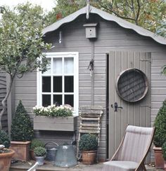 a small shed with potted plants and a chair in the foreground, outside